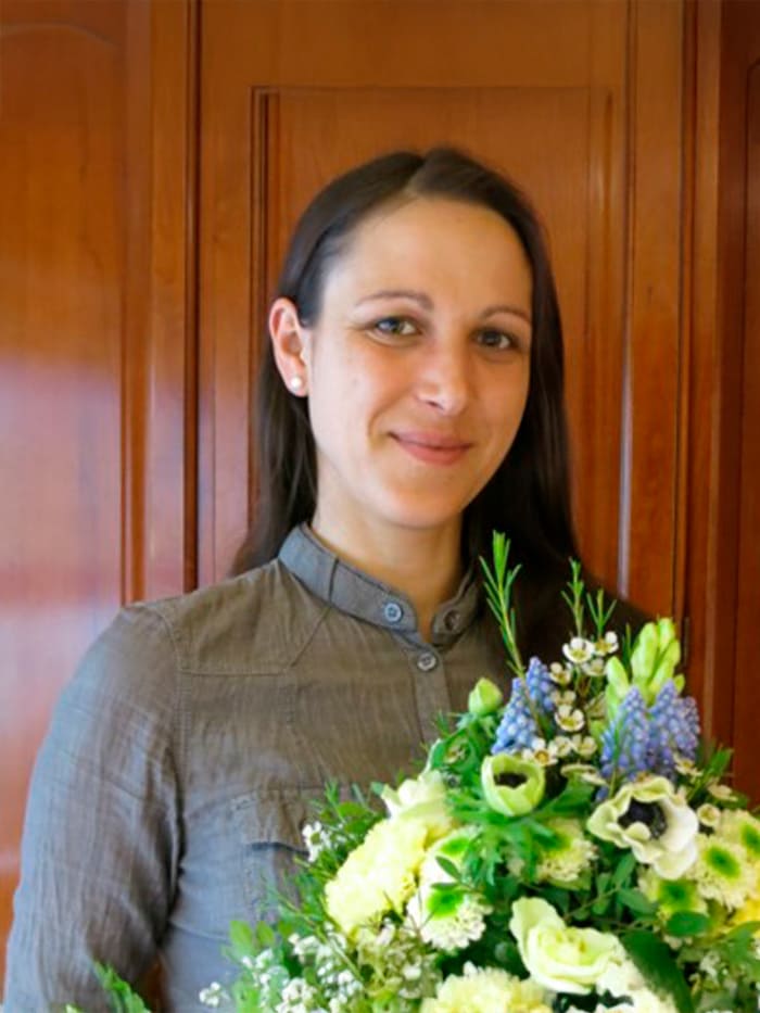 Eine Person steht vor einem hölzernen Hintergrund und hält einen Blumenstrauß in den Händen.
